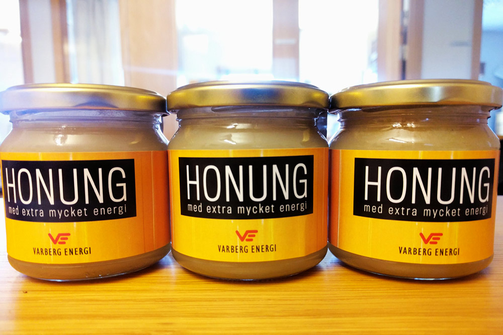 Tre honungsburkar med ordet honung och vår logotype på,står bredvid varandra