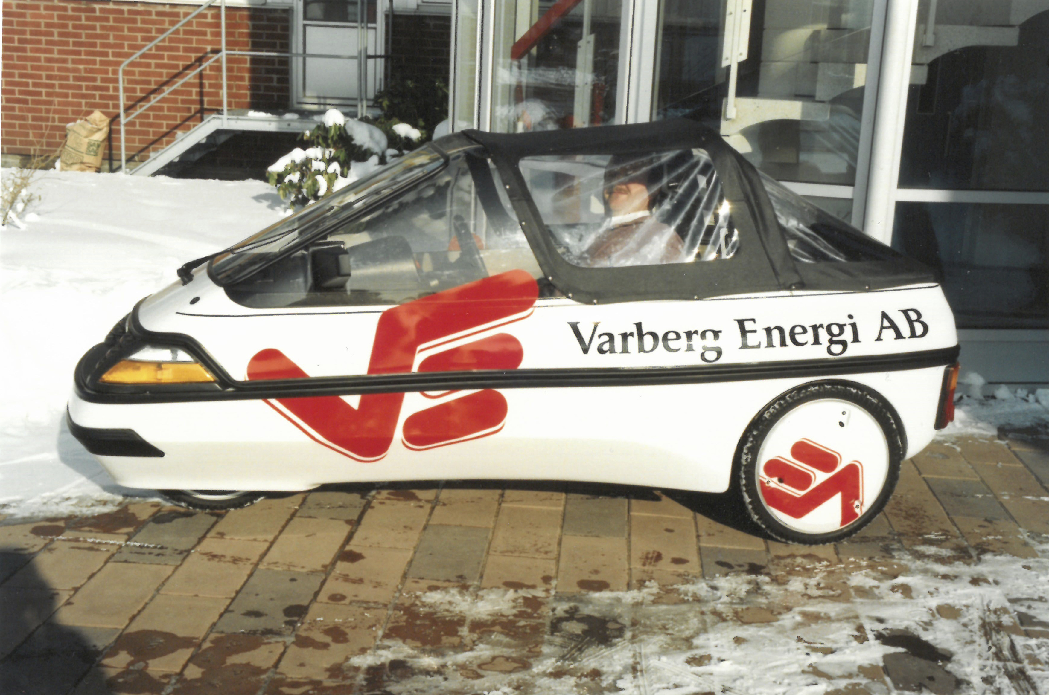 En liten vit ensitsig elbil med tre hjul och Varberg Energis logga på sidan.