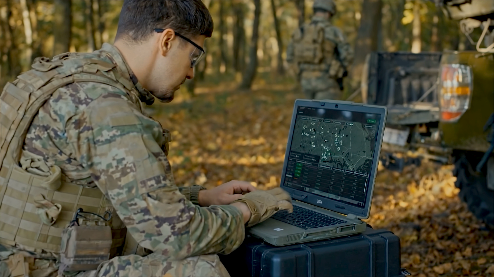 Kamouflageklädd soldat sitter i skogen med laptop och använder program.