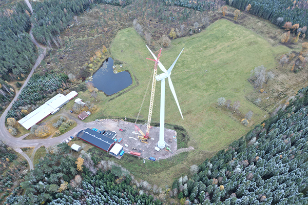flygbild över öppen plats med skog runt omkring och ett vindkraftverk i mitten.