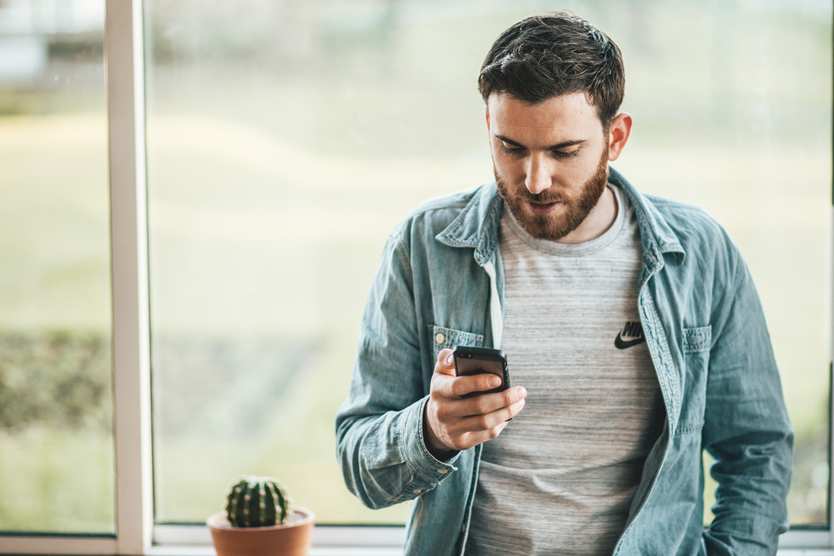 man står litad mot fönsterbräda och tittar i sin mobil